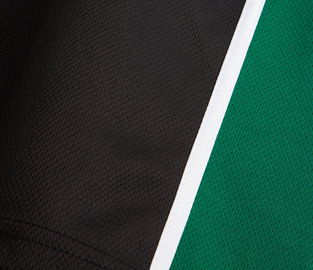 Close-up of SPIRIT Sports Polo - Black/Emerald, showcasing black and green textured knit panels separated by a white seam, highlighting its breathable Airmesh polyester fabric.